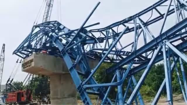 The buckled blue steel launcher girder folded over a concrete pier at the bridge construction site in Vaishali, with a crawler crane standing alongside.